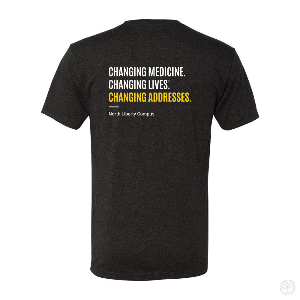 Back view of a dark gray t-shirt with white and yellow text that reads: ‘Changing Medicine. Changing Lives. Changing Addresses.’ with ‘North Liberty Campus’ printed below.